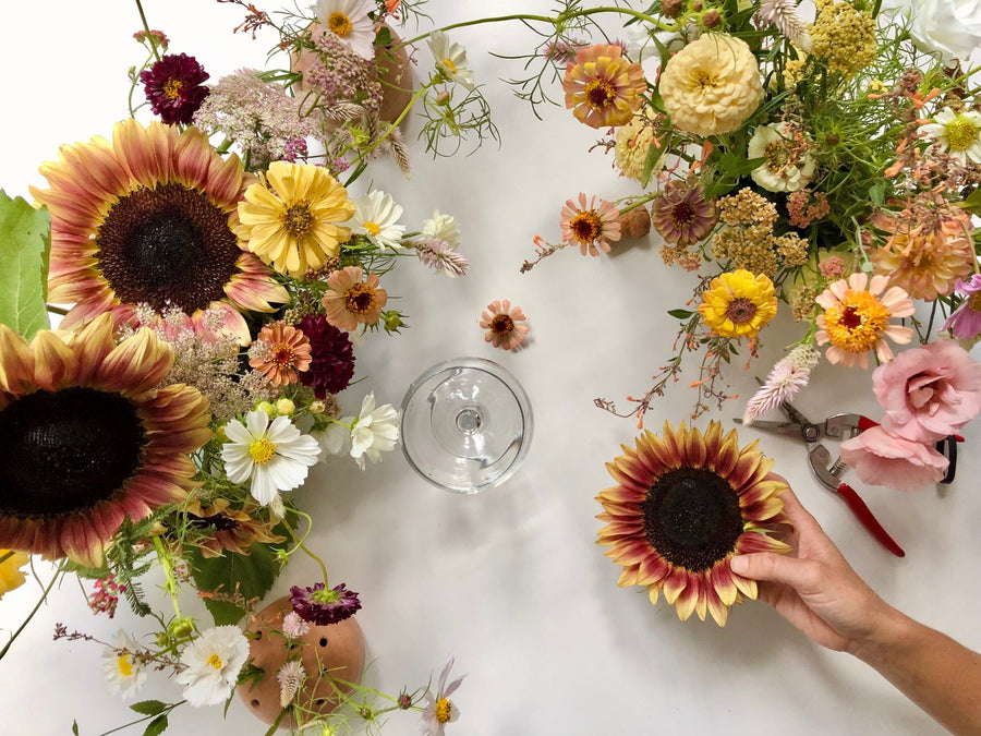 Arranging sunflowers and other flowers on a white surface with a glass of wine. Floral workshop example. 